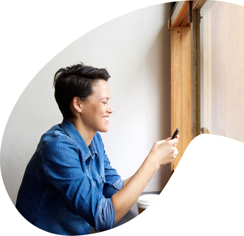 Profile of a smiling short-haired woman in a denim shirt looking at her smartphone in a cafe