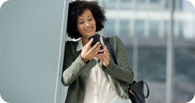 Smiling woman leaning against the wall while looking at her smartphone