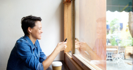 short-haired women happily looking at her phone in front of a window in a cafe